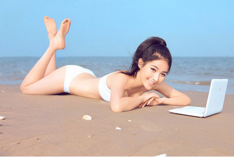 Người mẫu bikini dễ thương khoe dáng cùng máy tính bên bờ biển